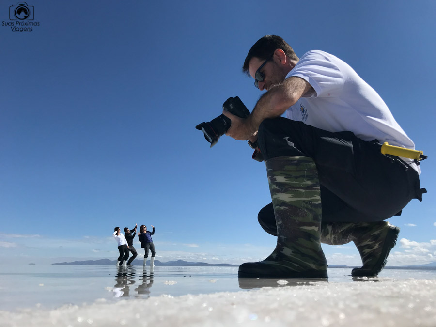 Imagem em perspectiva de um fotografo e pessoas distantes no salar de uyuni